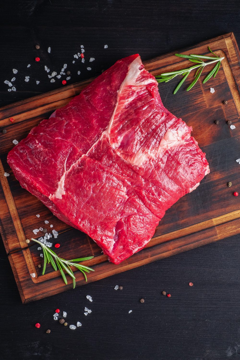 raw-meat-beef-steak-with-seasoning-on-chopping-board-on-dark-background-with-rosemary-.jpg